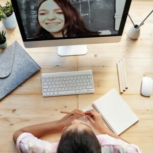 Teen girl participates in online class from home, focused on a computer screen with notebook.