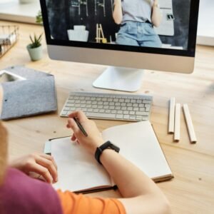 Student attending virtual class on a computer, taking notes at home.