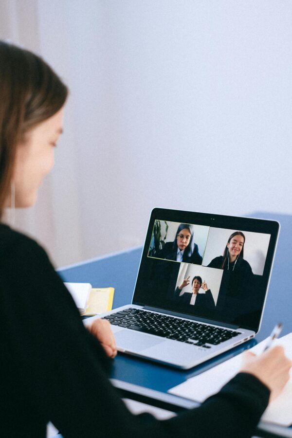 A woman participates in a virtual meeting with colleagues via video call on a laptop.